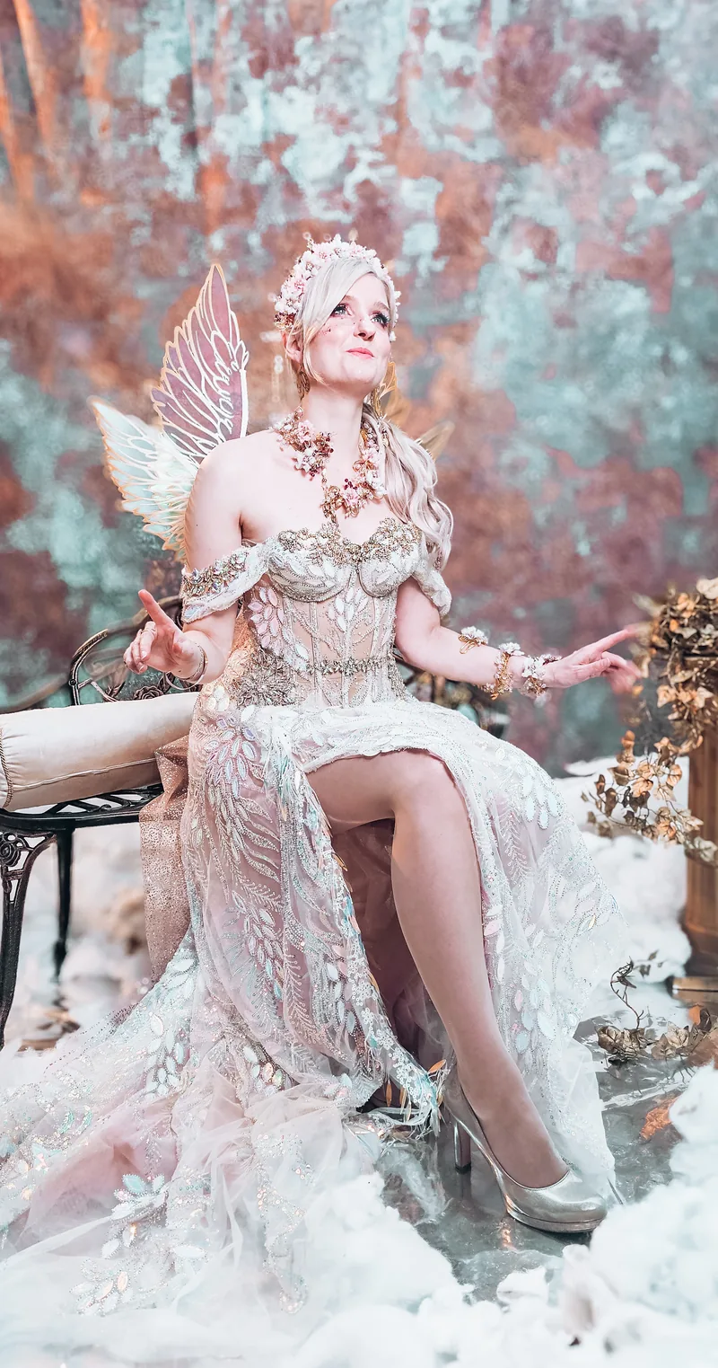 Laura sitzt in einem selbst gestalteten Fantasy-Kleid mit Flügeln in einer winterlichen Kulisse