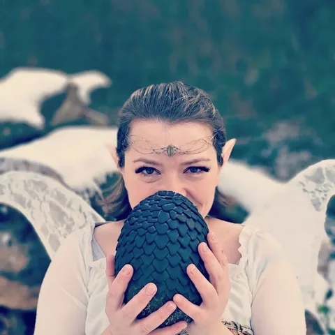 Jennifer mit Elfenohren hält ein dunkles Drachenei vor ihr Gesicht